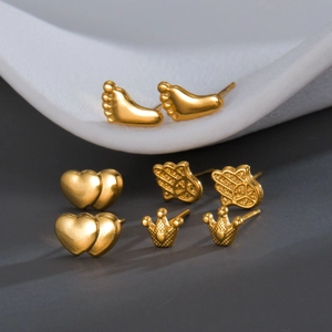 Set of four gold stainless steel bee and hamsa ear studs on minimalist background