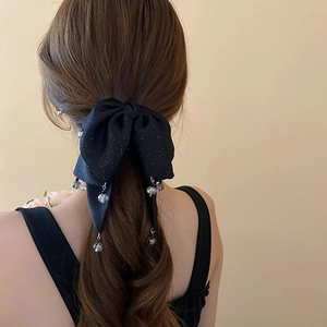 Detail of a black bow hair clip with silver sparkles and a clear bead pendant on brown hair