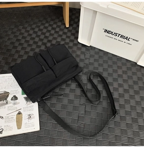 Flat lay of a black nylon crossbody bag with multiple pockets on a textured mesh mat