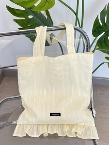 Chic beige quilted canvas tote bag with ruffle trim and shoulder strap on a chair