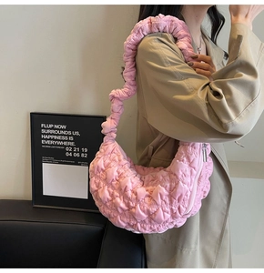 Pink quilted cloud bag with pleated shoulder strap worn by a model in a minimal room