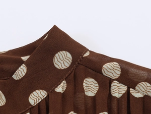 Detailed close-up of dark brown mock neck collar with white polka dots and pleated design