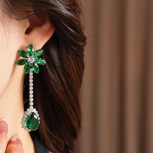 Close-up of elegant long zircon floral tassel earrings with green teardrop stones on a model
