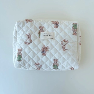 Detail of white quilted teddy bear cosmetic bag featuring woven label and soft cotton texture