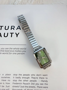 Macro detail of silver rectangular quartz watch with green dial on vintage book pages