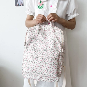 Detailed shot of a floral canvas backpack with pink flowers held by a model in a white dress