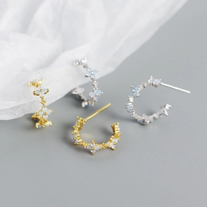 Detailed view of silver and gold C-shaped earrings with white clover-shaped stones
