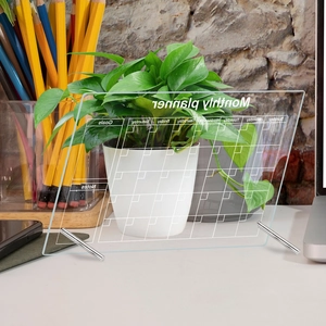 Clear acrylic monthly planner board with metal stand on desk for office organization