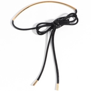 Detail of a gold tube necktie choker with a black cord bow and elegant gold end caps