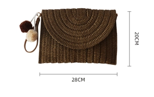 Detail view of brown woven straw clutch bag with colorful pompom charms and 28x20cm size