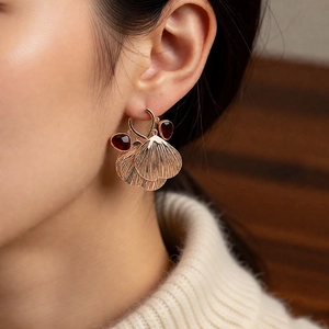 Close-up of rose gold fan earrings with dark red drop gems worn by a model