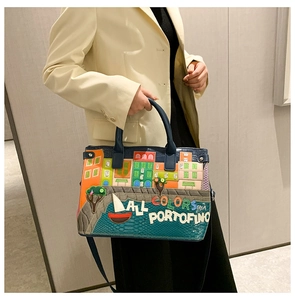 Detail of Portofino embroidery on blue embossed leather handbag held by model