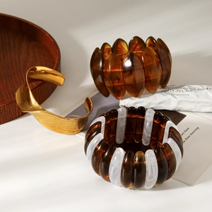 Detailed close-up of golden textured cuff and amber resin beaded bracelets on white table