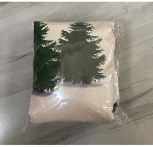 Close-up of beige linen Christmas tree skirt with green pine tree patterns in packaging