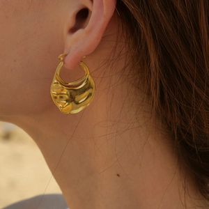 Dettaglio degli orecchini in oro 18K con texture lavica indossati da una modella