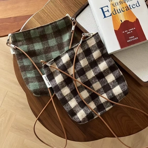 Detailed close-up of two plaid wool crossbody bags with leather straps on a wooden table