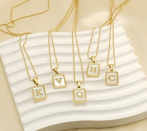 Detail of square gold pendants with K V Q H C initials on white textured board