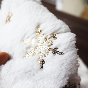 Macro detail of white faux rabbit fur Christmas tree skirt with golden sequin snowflakes