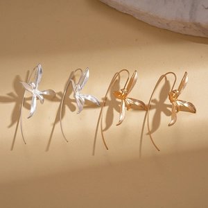 Golden and silver iris flower drop earrings with long hooks on a stone surface