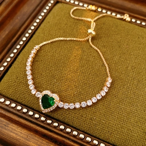 Detail view of adjustable gold heart bracelet with green stone and square zircons