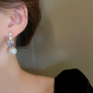 Close-up of elegant knotted silver needle earrings with zircon and pearl on model