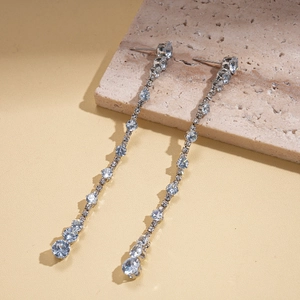 Close-up of silver tassel earrings with clear zircons on a textured stone surface