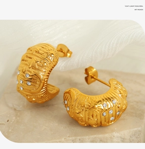 Macro shot of gold C-shape hoop earrings with embossed stars, moons and tiny rhinestones