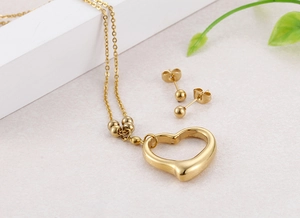 Detail view of gold heart pendant necklace and ball stud earrings on a textured surface