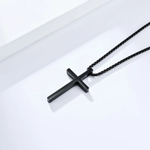 Close-up of minimalist black cross pendant necklace with matching black chain on white background
