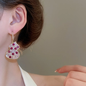Macro shot of gold gourd drop earring with sparkling white zircons and red main stones