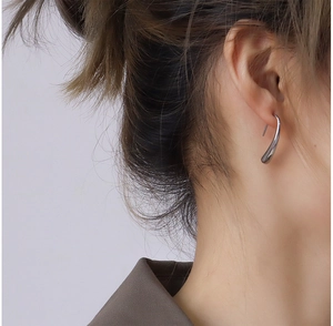 Close-up of polished silver teardrop hook earrings worn by a model in soft lighting