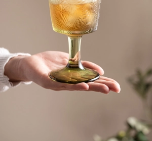 Close-up of green vintage glass goblet with leaf texture held by hand in warm lighting