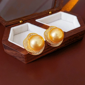 Detailed close-up of a golden pearl earring with crystal halo in a premium wooden jewelry box