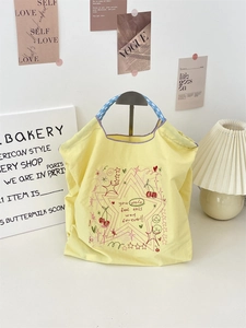 Detail of yellow embroidered tote bag with cherry prints and blue checkered handles