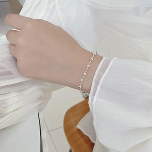 Dettaglio del bracciale con perle d'argento sul polso su morbido tessuto bianco