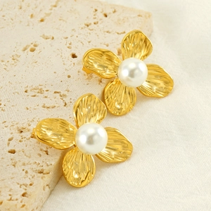 Detail view of gold flower earrings with ribbed texture and central pearl on stone