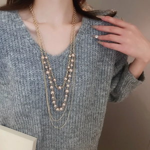 Close-up of elegant multi-layer gold chain necklace with pearls on a grey sweater
