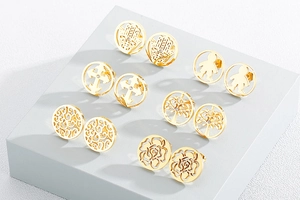 Close-up of gold hollow earrings set featuring cross and tree of life on stone display