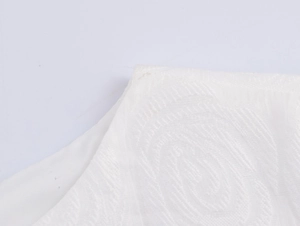 Close-up of white textured jacquard fabric showing elegant floral cutout details