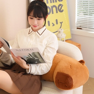 Long capybara plush pillow held by a person on a cozy sofa in a warm living room