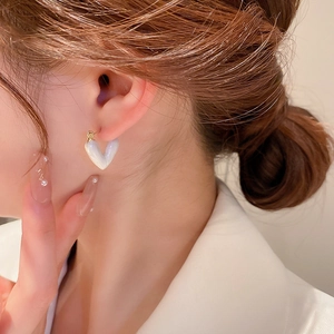 Detail of heart-shaped earring with pearlescent finish and gold hook on a model