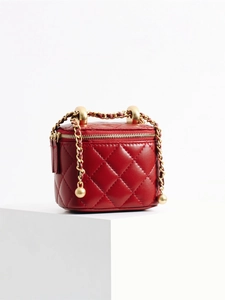 Red quilted leather cosmetic handbag with gold chain handle on white pedestal