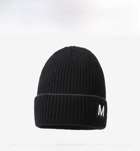 Detail of black ribbed knit beanie featuring white letter M patch and soft texture