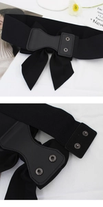 Detail of black elastic wide waist belt featuring a large bow and metallic SN snap buttons