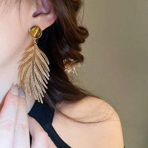 Close-up of vintage feather-shaped gold earrings with round tiger eye stone on model