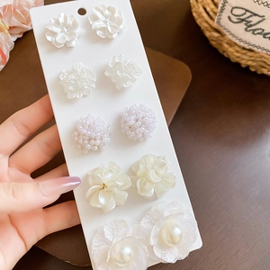 Detailed close-up of 5 pairs of floral pearl earrings with white acrylic petals