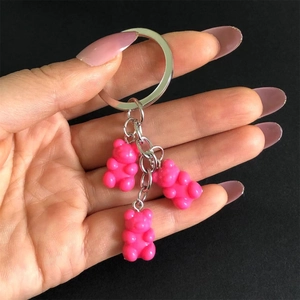 Pink cartoon resin bear keychain pendant with three charms and metal ring on dark backdrop