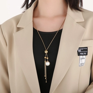 Dettaglio della collana dorata con nappa e perla indossata su un blazer elegante