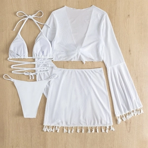 Flat lay of white four-piece bikini set with tassel skirt and mesh cover-up top on wood