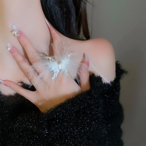 Close-up of white feather butterfly ring with sparkling rhinestones worn on index finger